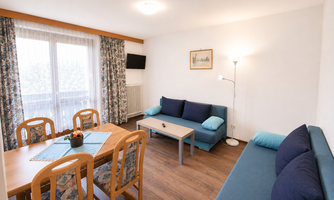 A cozy living space with a table and four chairs. The seating area features a blue couch and plenty of daylight through the window.