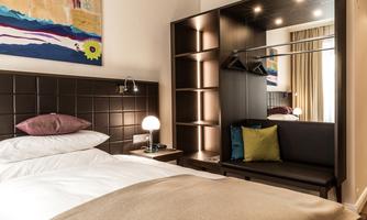 A modern bedroom with a bed, a cozy seating area, and a stylish wardrobe. The decor is elegantly and minimally designed.