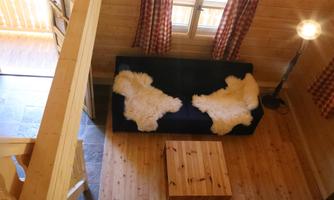 A cozy room with a blue couch and two sheep skins. A wooden table and a floor lamp complement the decor.