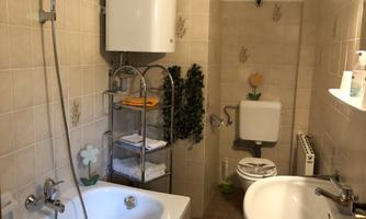 A small bathroom with a bathtub, a sink, and a toilet. The walls are tiled in light colors, and the furnishings are functional.