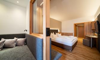 A modern hotel room with wooden interior and a cozy seating area. The room features a large bed and elegant decor.