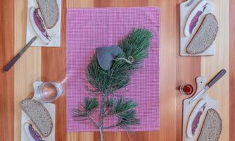 A laid table with a wooden surface, on which bread and a glass of water are placed. In the center lies a green twig and a gray decoration.