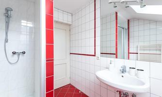 A modern bathroom with white tiles and red accents. It features a shower, a sink, and a large mirror.