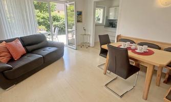 A bright living room with a comfortable sofa and a dining table. Large windows offer a view of the garden.