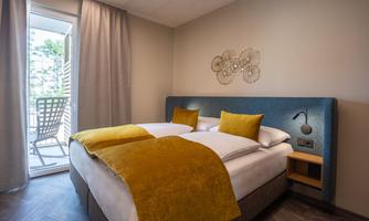 A modern hotel room with a large bed and yellow pillows. There is access to a small balcony with a view.