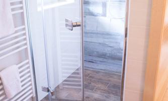 A modern bathroom with an elegant shower area and bright wooden flooring. The clear shower wall and large tiles give the space a fresh, clean look.
