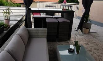 An elegant terrace with a covered seating area and modern furniture. In the background, there are plants and a bar that invites relaxation.