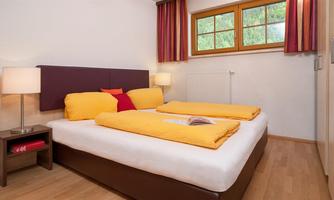 A cozy bedroom with two single beds that have yellow bedding. The room is bright and has large windows that let in daylight.