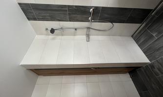 A modern shower with white and gray tiles. The wall is equipped with a wooden panel and a showerhead.