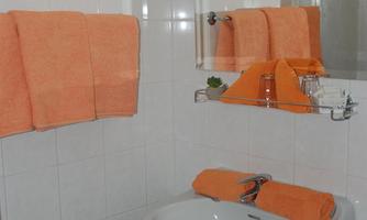 A small bathroom with white tiles and orange towels. The furnishings include a sink and a trash can.