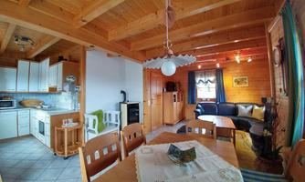 A cozy living area with an open kitchen and wooden ceilings. The space is bright and inviting, featuring a dining area and a comfortable couch.