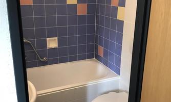 A simple bathroom with a bathtub and colorful tile design. The toilet is located near the bathtub.