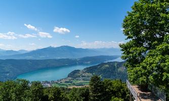 A picturesque view of a clear lake with mountains in the background. The sky is blue and filled with sunlight.