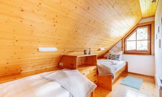 A cozy bedroom with two single beds and wooden paneling. A window provides plenty of light and a view of the outdoors.
