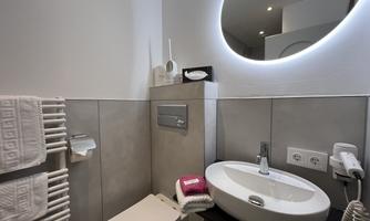 A modern bathroom with a round mirror and a sink. Towels and a hairdryer are also available.