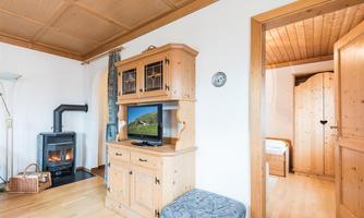 A cozy room with wooden shelves and a television. In the background, there is a wood stove and an open door leading to another room.