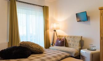 A modern bedroom with a cozy bed, a beautiful lamp, and a small television on the wall. The windows are decorated with elegant curtains, and the room feels bright and inviting.