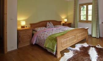 A cozy bedroom with a large double bed and wooden furniture. The walls are painted in a soft green hue, and a carpet adds extra comfort.