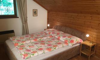 A cozy bedroom with a large double bed. The walls are made of wood, and a window allows daylight to come in.