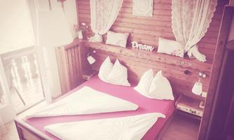 A cozy bedroom with a double bed and pink bedding. Decorative curtains hang on the wall and there is a sign that reads "Dream."
