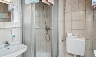 A modern bathroom with a shower, sink, and toilet. The walls are tiled, and a wooden ceiling creates a cozy atmosphere.