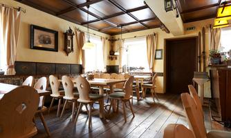 An inviting restaurant with wooden tables and chairs. Windows with curtains let in plenty of daylight.