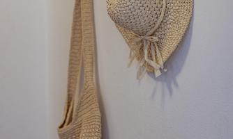 A straw-colored bag hangs next to a sun hat on the wall. They are both attached to decorative hooks.