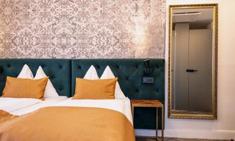 A stylish bedroom with a green headboard and orange pillows. Next to the bed is a mirror with an elegant golden frame.