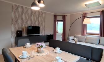 A modern dining area with a wooden tray and stylish chairs. The bright apartment has large windows and a cozy atmosphere.