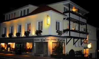 A guesthouse with a light yellow facade and a lit entrance. In front of the building, windows are decorated with plants.