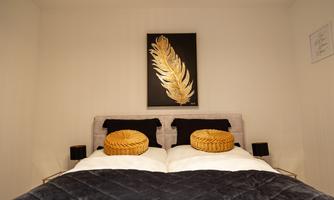 An elegant bedroom with a double bed and two golden pillows. A modern artwork with a golden leaf hangs on the wall.
