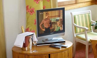 A television stands on a wooden side table in a room. Next to the television is a champagne bottle in an ice bucket and a glass.