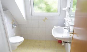 A small, bright bathroom with a sink and a toilet. There is a window that lets in daylight.