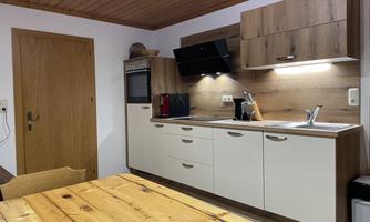 A modern kitchen with wooden shelves and a bright countertop. In the foreground stands a large wooden dining table.