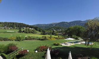 A beautiful garden with green meadows and blooming plants. In the background, mountains and a blue sky can be seen.