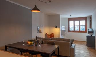 A modern living room with a cozy sofa and a dining table. Large windows allow for plenty of light and a friendly atmosphere.