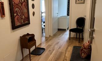 A bright hallway with wooden flooring. Pictures are hanging on the wall, and there is a small seating area.