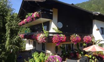 A beautiful house with a balcony adorned with colorful plants. In the foreground, there are cozy seating options and a sun umbrella.