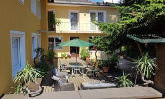 A cozy courtyard with a table and chairs under a sunshade. Surrounded by plants and a yellow wall, the place seems inviting and friendly.