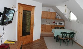 A cozy room with an open kitchen and a dining area. The furniture is made of wood and the room has a bright, inviting atmosphere.