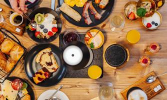 A beautifully set table with various breakfast dishes. On the plates, there are eggs, bacon, fruits, croissants, and drinks.