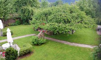 A green garden landscape with a large tree and hilly views in the background. A cozy spot with garden furniture is also visible.