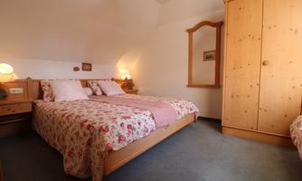 A cozy bedroom with a large bed and flower-shaped bed linen. The room is bright and features a wooden wardrobe as well as a mirror.