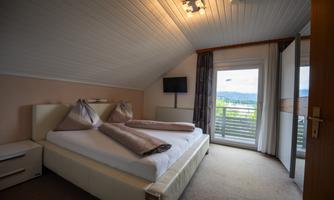 A cozy bedroom with a large bed and two pillows.  
Large windows offer a view outside and plenty of daylight.