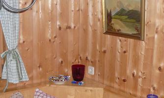 A cozy room with wooden walls and a picturesque picture on the wall. On a shelf, there are some sweets and a red glass.