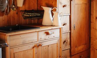 A cozy kitchen with wooden shelves and rustic furniture. A white pitcher is on the countertop next to a sink.