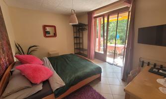 A cozy bedroom with a double bed, colorful pillows, and a large window. The terrace offers a view of the greenery.