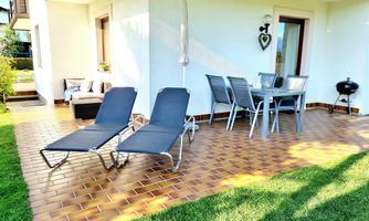 A cozy patio with two loungers and a dining table. The terrace is surrounded by green grass and offers an inviting outdoor space.