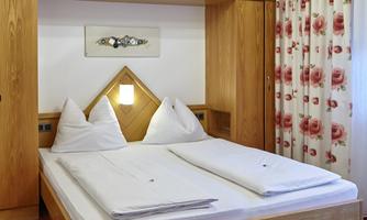 A cozy bedroom with a double bed and wooden furniture. The walls are decorated with floral-patterned wallpaper.