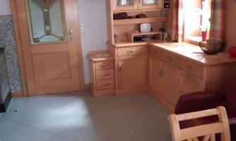 A bright kitchen with wooden furniture and a large window. The room is simply and comfortably furnished.